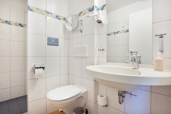 A bathroom with a toilet, sink, mirror, and towel dispenser. - Vollmöblierte Wohnungen in Münster (Münster)