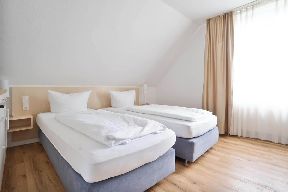 A hotel room with two beds, a wooden floor, a headboard, and a window with curtains.