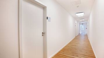 A corridor with white walls, wooden flooring, and a door with a sign.