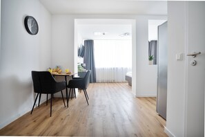 A modern dining area with a wooden floor, two black chairs, a table with a fruit bowl, and a clock on the wall. - Vollmöblierte Wohnungen in Münster (Münster)