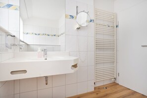 Baño con lavamanos, espejo, toallero y piso de madera.