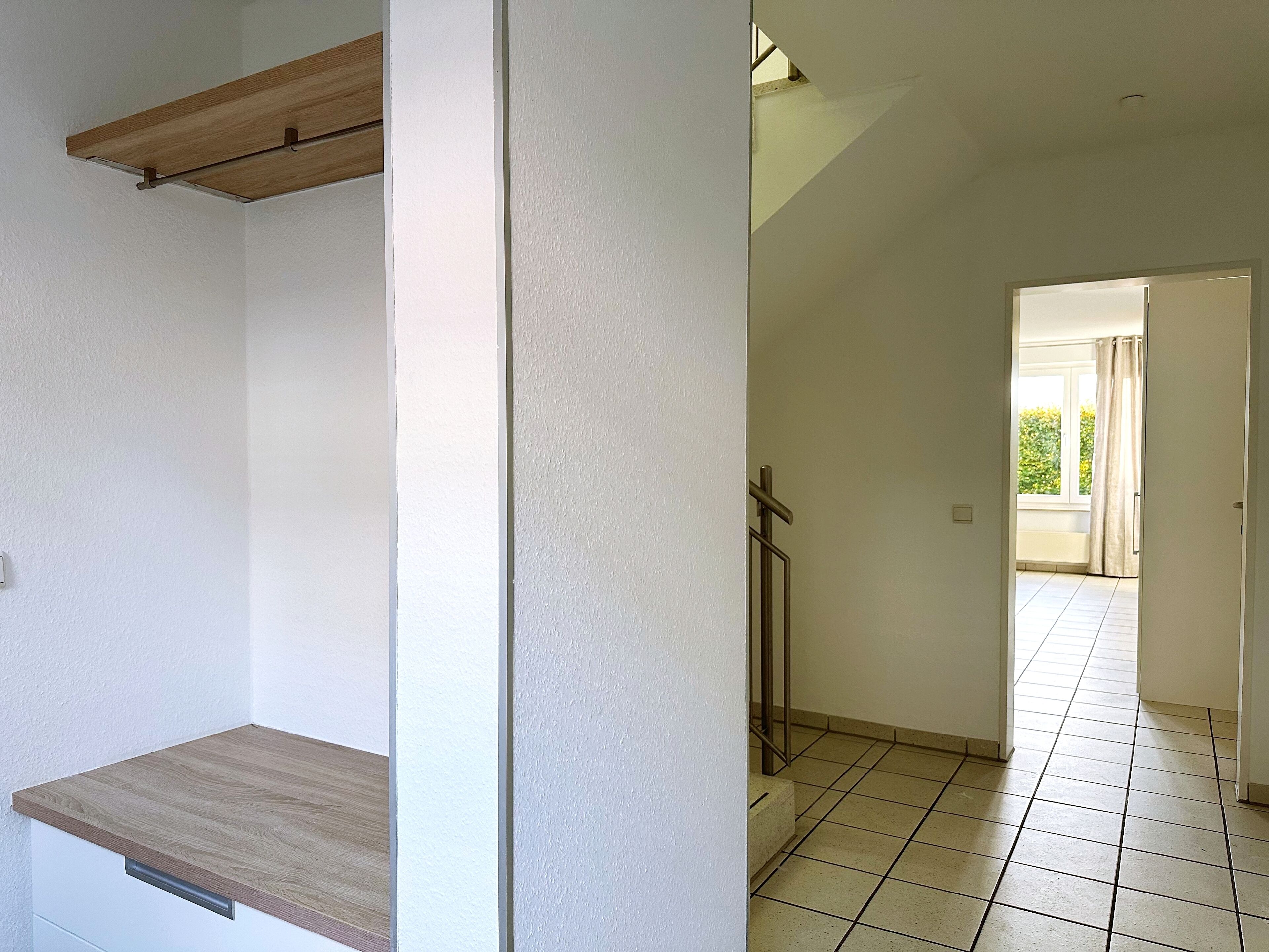 A hallway with a wooden shelf, a door leading to a balcony, and tiled flooring.