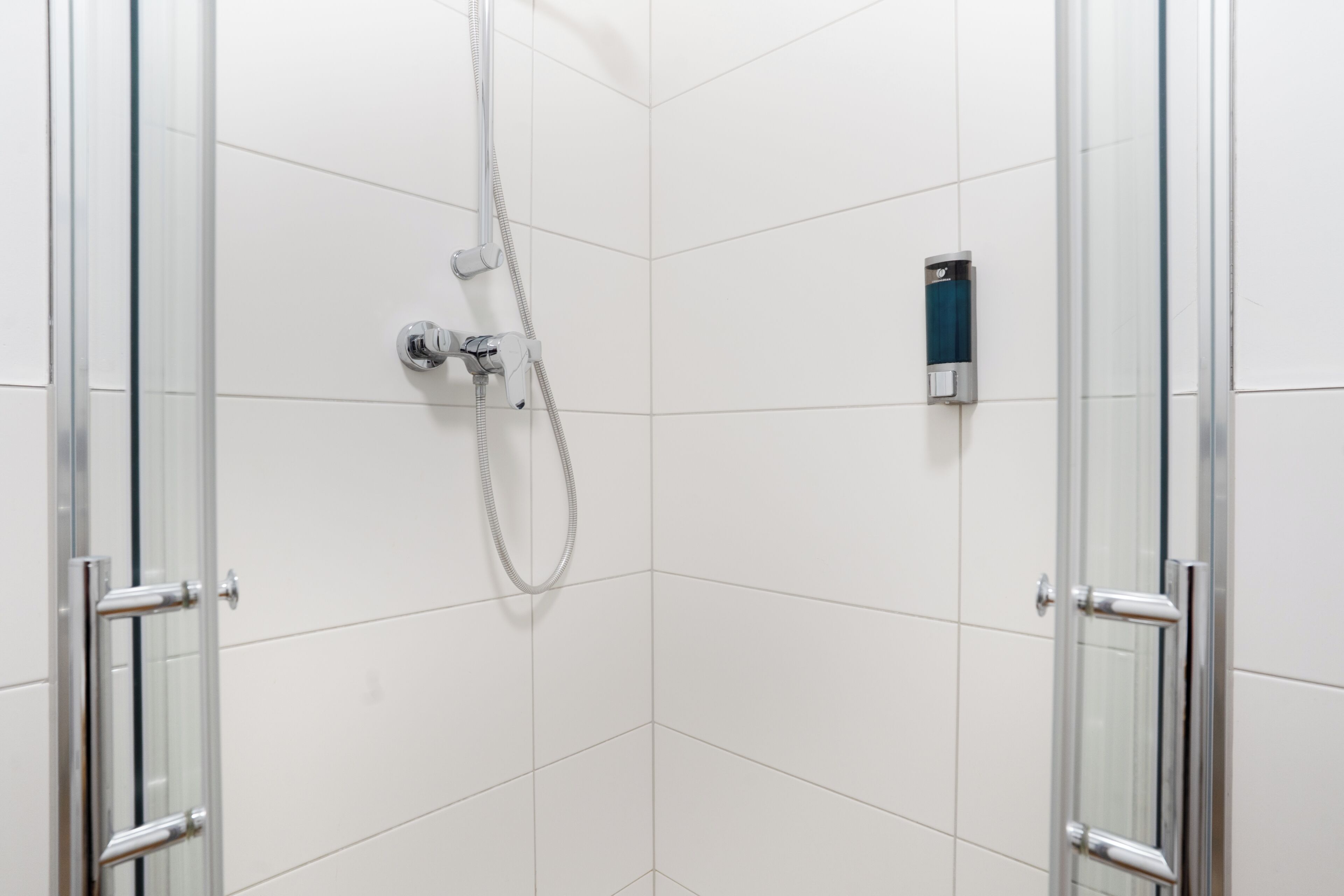 Um chuveiro com divisória de vidro, um chuveiro manual e um painel de controle fixado na parede.