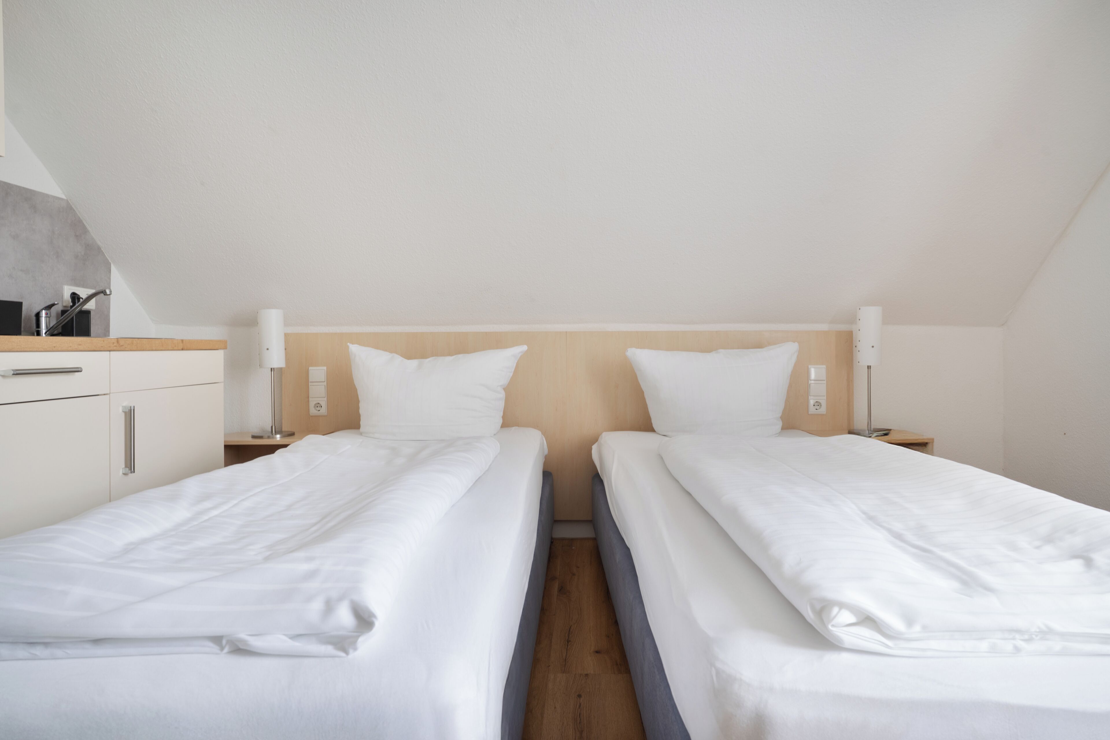 A twin room with two beds, a wooden headboard, bedside lamps, a small table, and a built-in cabinet.