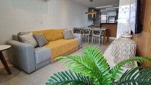 A modern living room with a sofa, a dining table with chairs, and a kitchen area in the background. - Flat 306 Villa Hípica Gravata (Gravata)