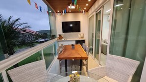 A balcony with a wooden table and wicker chairs, a flat-screen TV, and a view of the landscape. - Flat 306 Villa Hípica Gravata (Gravata)