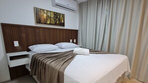 A hotel room with a wooden headboard, a bed with white bedding, a brown throw blanket, a white pillow, a nightstand, and an air conditioning unit. - Flat 306 Villa Hípica Gravata (Gravata)