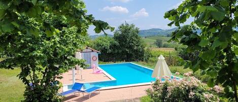 A swimming pool surrounded by lush greenery, with a small gazebo and lounge chairs.