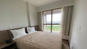 A hotel room with a bed, a bedside table with a phone, and a window with curtains.