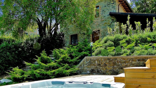 A hot tub surrounded by lush greenery and a stone wall, with a rustic building in the background. -  Silvio, Beautifully presented villa with own pool and hot tub. (Filicaia)