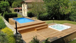 A wooden deck with a hot tub and a swimming pool, surrounded by greenery and a house in the background. -  Silvio, Beautifully presented villa with own pool and hot tub. (Filicaia)