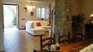 A dining area with a wooden table, chairs, and a plate of food. There is a white sofa and a stone wall in the background. -  Silvio, Beautifully presented villa with own pool and hot tub. (Filicaia)