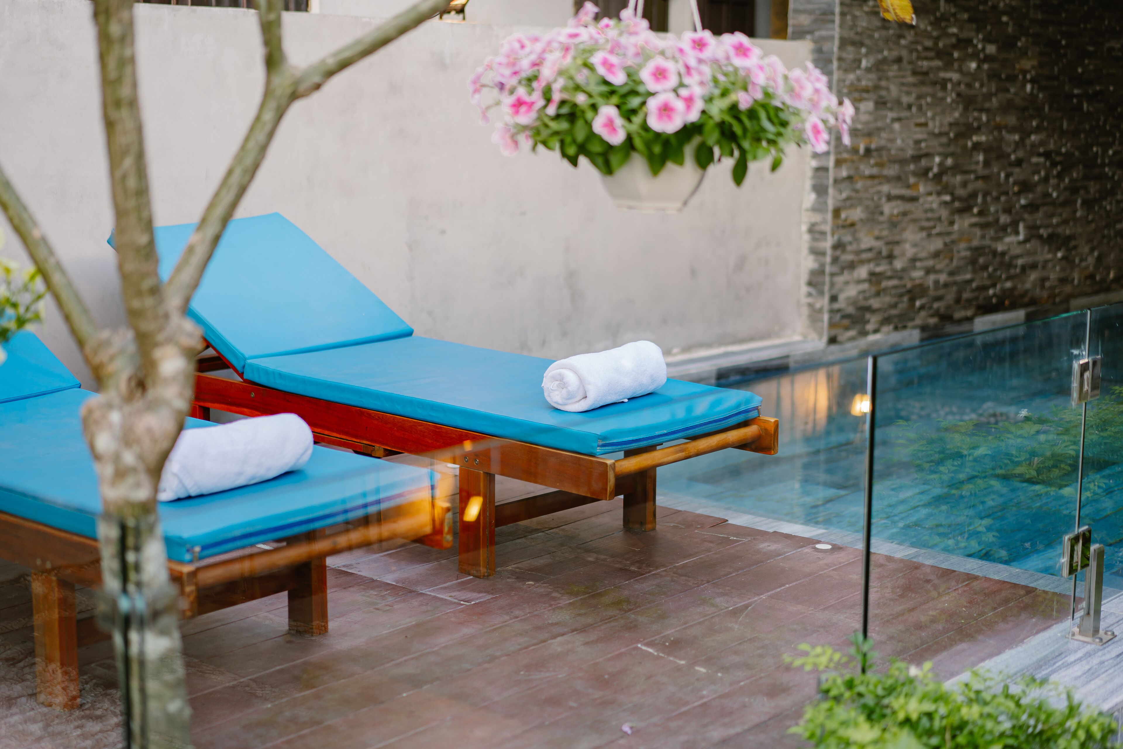 Un espace aménagé au bord de la piscine, avec deux chaises longues, une rouge et une bleue, toutes deux accompagnées de serviettes blanches.