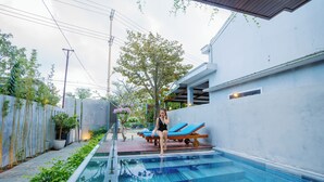 A swimming pool with steps, a person sitting on the edge, and a tree in the background. - LaSanta Villa (Da Nang)