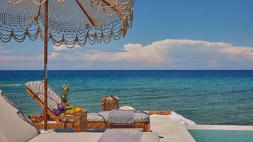 A luxurious seaside lounge with a wooden bench, a small table with fruits and flowers, and a netted umbrella.