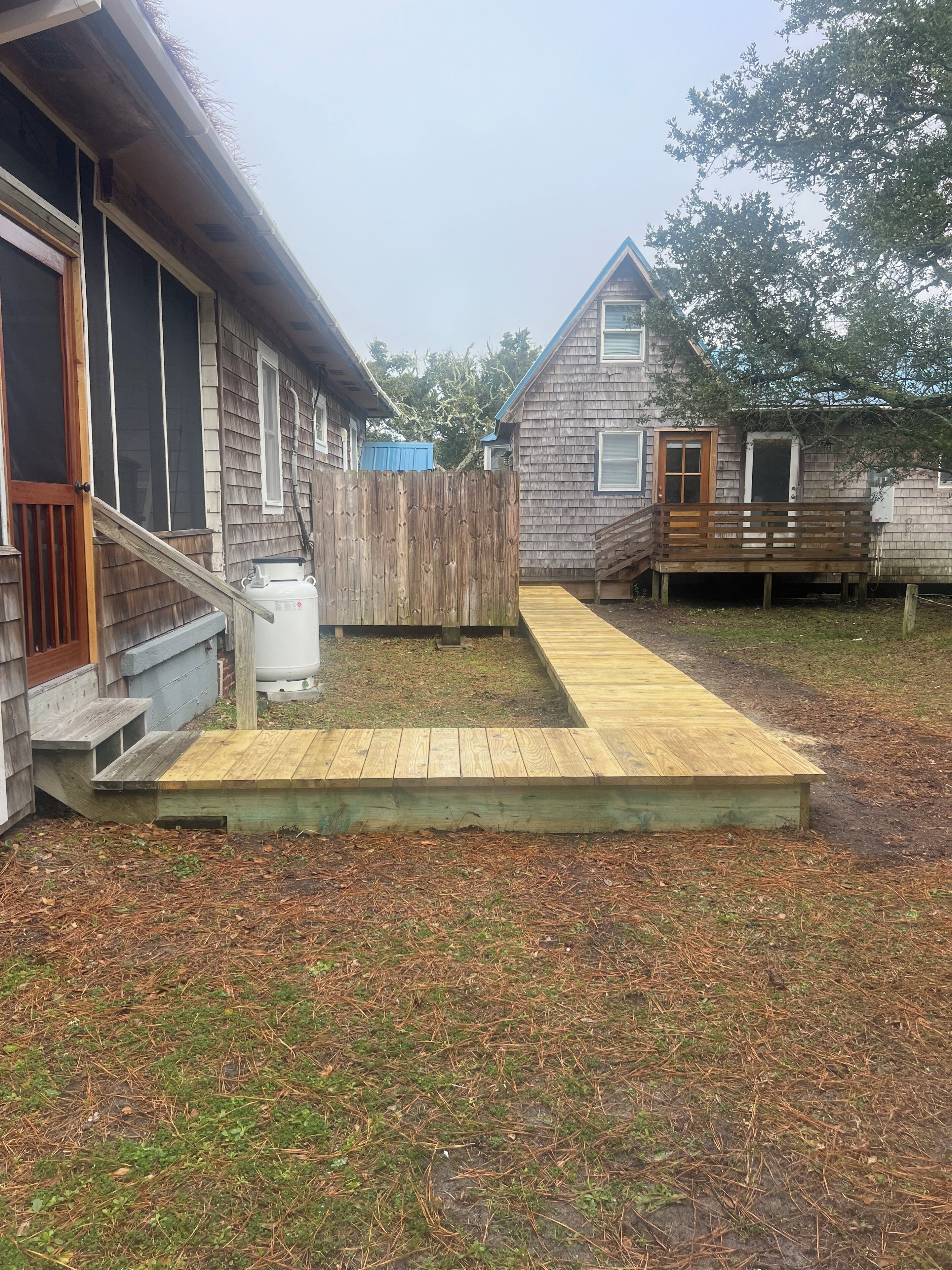 A wooden deck leading to a house with a porch and a fenced yard.