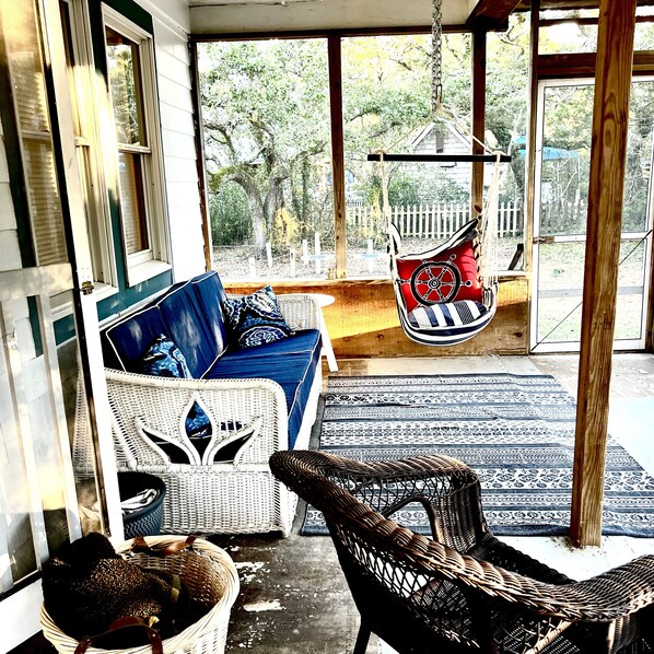 A porch with wicker furniture, a hanging chair, and a view of the outdoors.