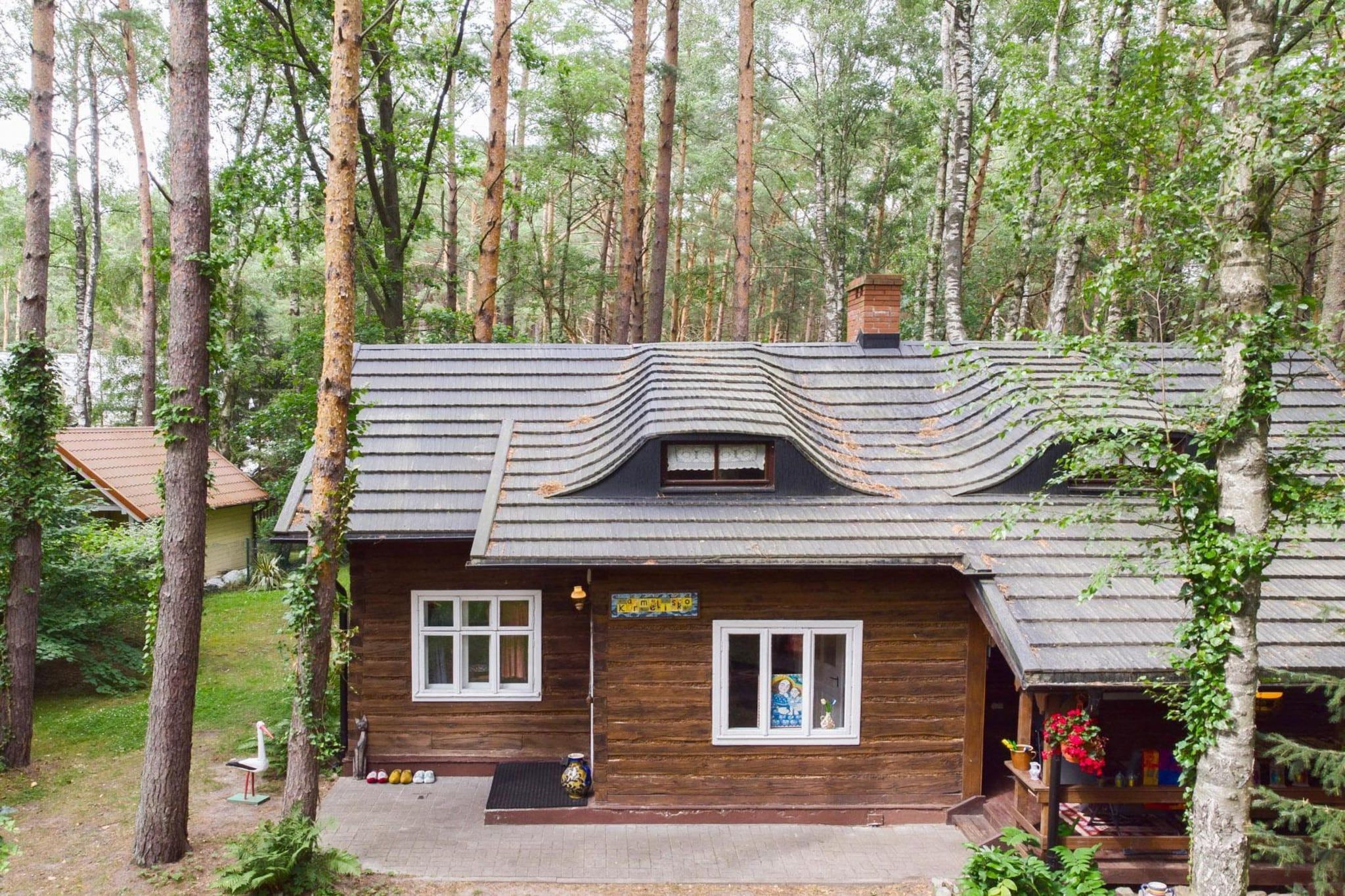 A wooden cabin with a unique wavy roof design, surrounded by a forest.