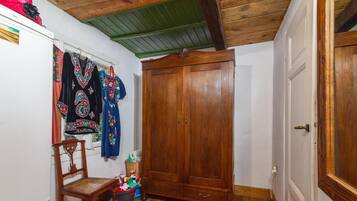 Une pièce avec une armoire en bois, une chaise, un tapis rouge et un mur où sont suspendus des vêtements.