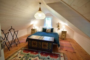 Une chambre confortable située dans les combles, avec un lit, deux tables de chevet, un luminaire suspendu et une fenêtre.