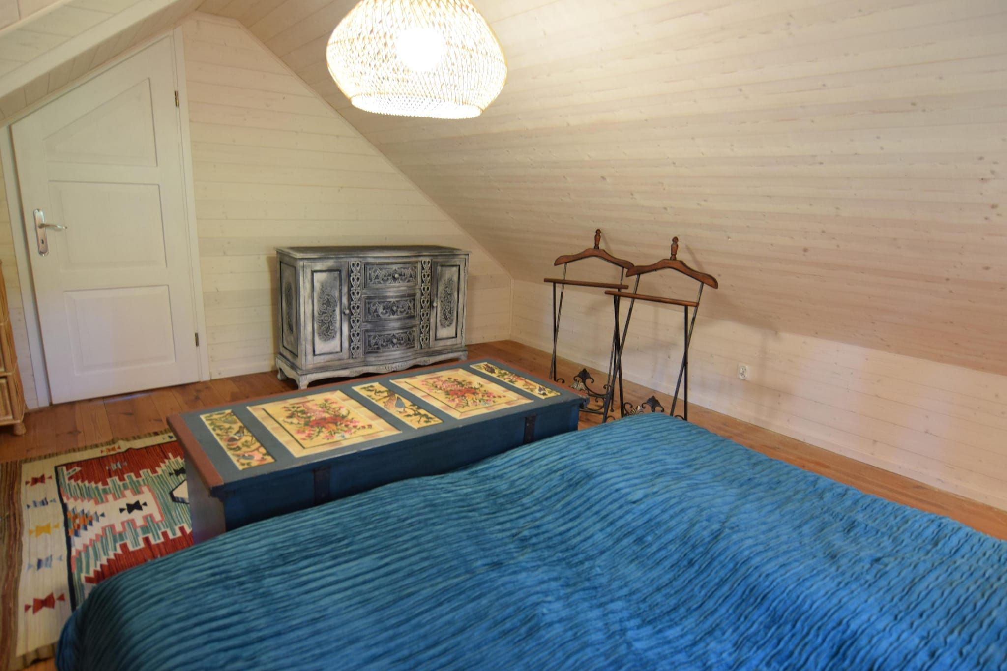 A bedroom with a bed, a dresser, a hanging rack, and a patterned rug.