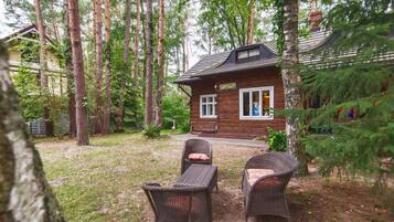 Une cabane en bois dotée d’un porche, entourée de grands arbres et bordée d’une pelouse.