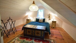 A cozy attic bedroom with a sloped ceiling, a large bed with a patterned headboard, two bedside tables with lamps, and a hanging light fixture.