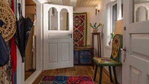 A hallway with a white door, a patterned rug, a chair, and a decorative wall piece.