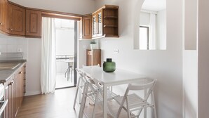 Une cuisine avec des meubles en bois, un plan de travail blanc et un coin repas avec des chaises blanches.