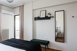A bedroom with a bed, a bedside table, a mirror, a shelf with decorative items, and a radiator. - Signature 2BR Apartment in Marousi (Marousi)