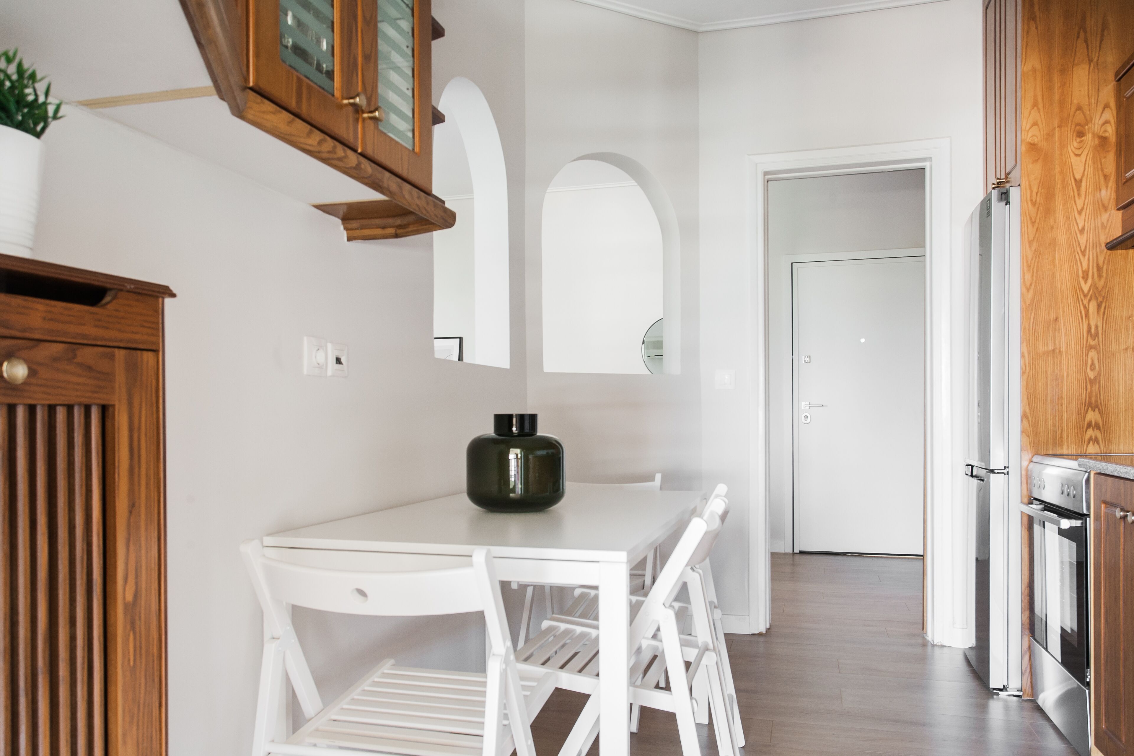 A modern kitchen with white cabinetry, a dining table with chairs, and a built-in oven.