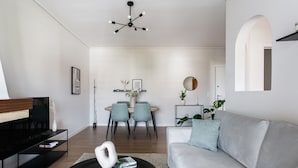 Un salon moderne avec un canapé gris, une table basse noire et un coin repas comprenant une table ronde et des chaises bleues.