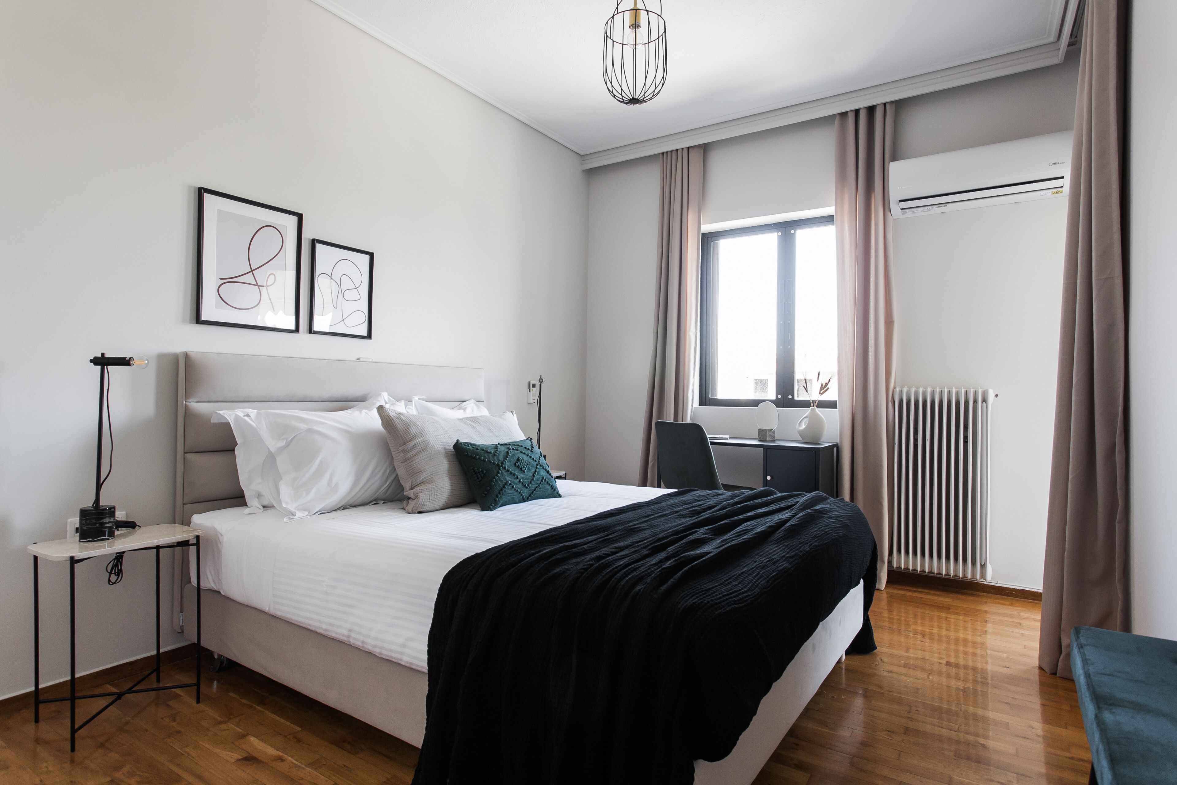 A modern bedroom with a large bed, a bedside table, a desk, and a window with curtains.