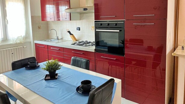 Cozinha compacta com armários vermelhos, fogão a gás e forno embutido.