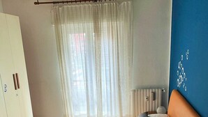 Quarto com cama, guarda-roupa, ventoinha no teto e janela com cortinas.