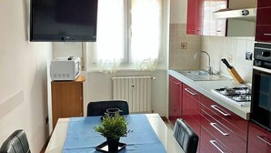 Uma cozinha compacta com área de jantar, uma TV de tela plana fixada acima do balcão e uma janela com cortinas.