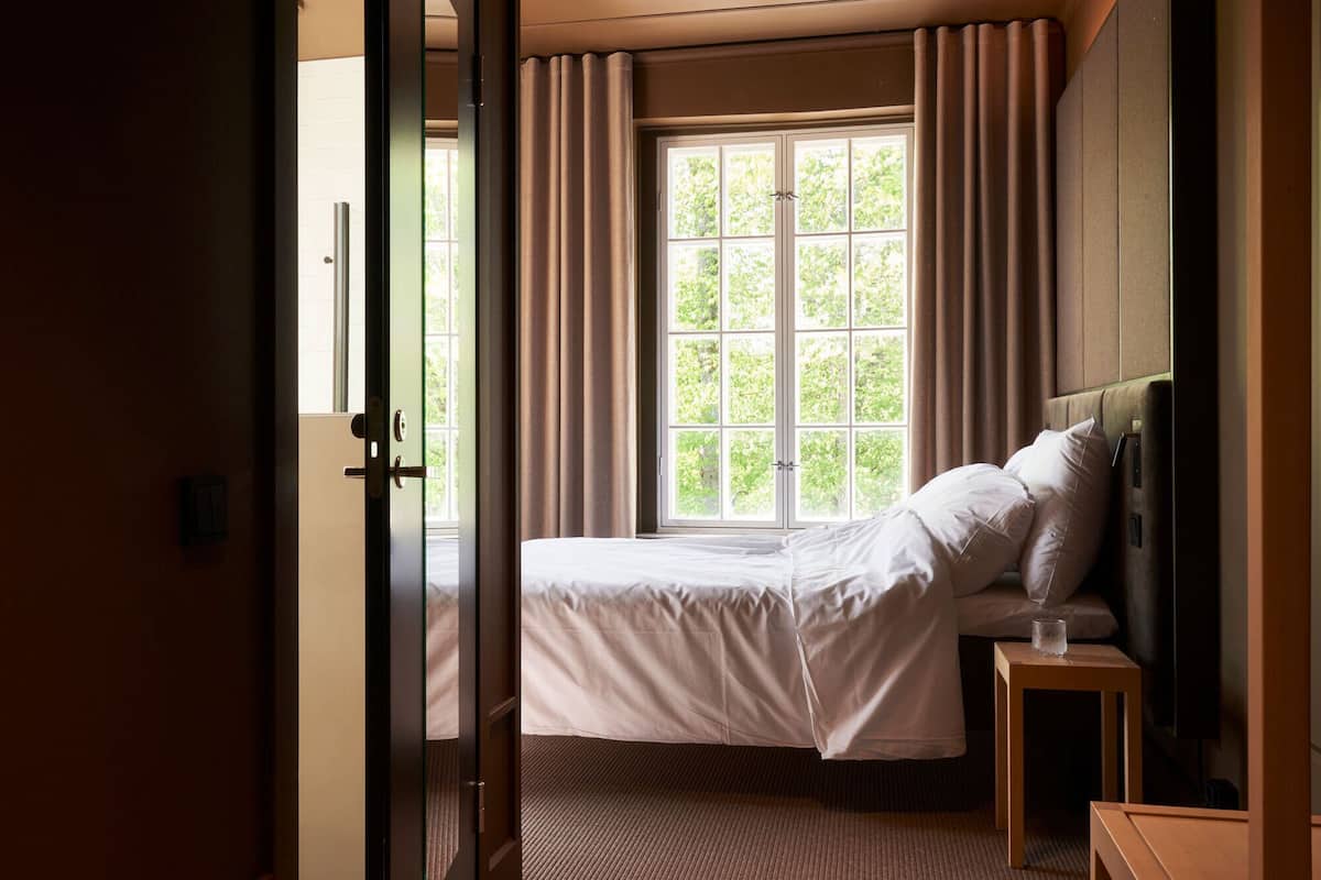 A hotel room with a large window, a bed, a bedside table, and a television.
