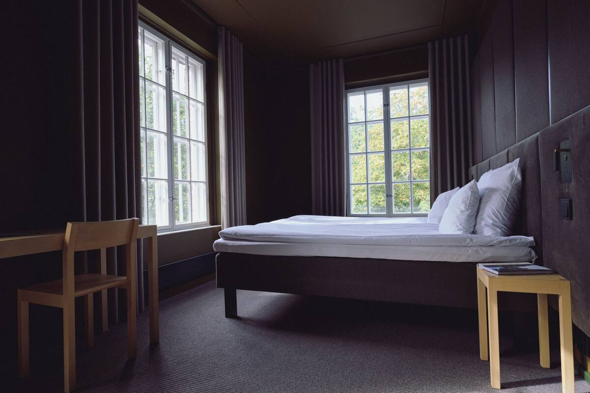 A bedroom with a bed, a desk, and a window with curtains.