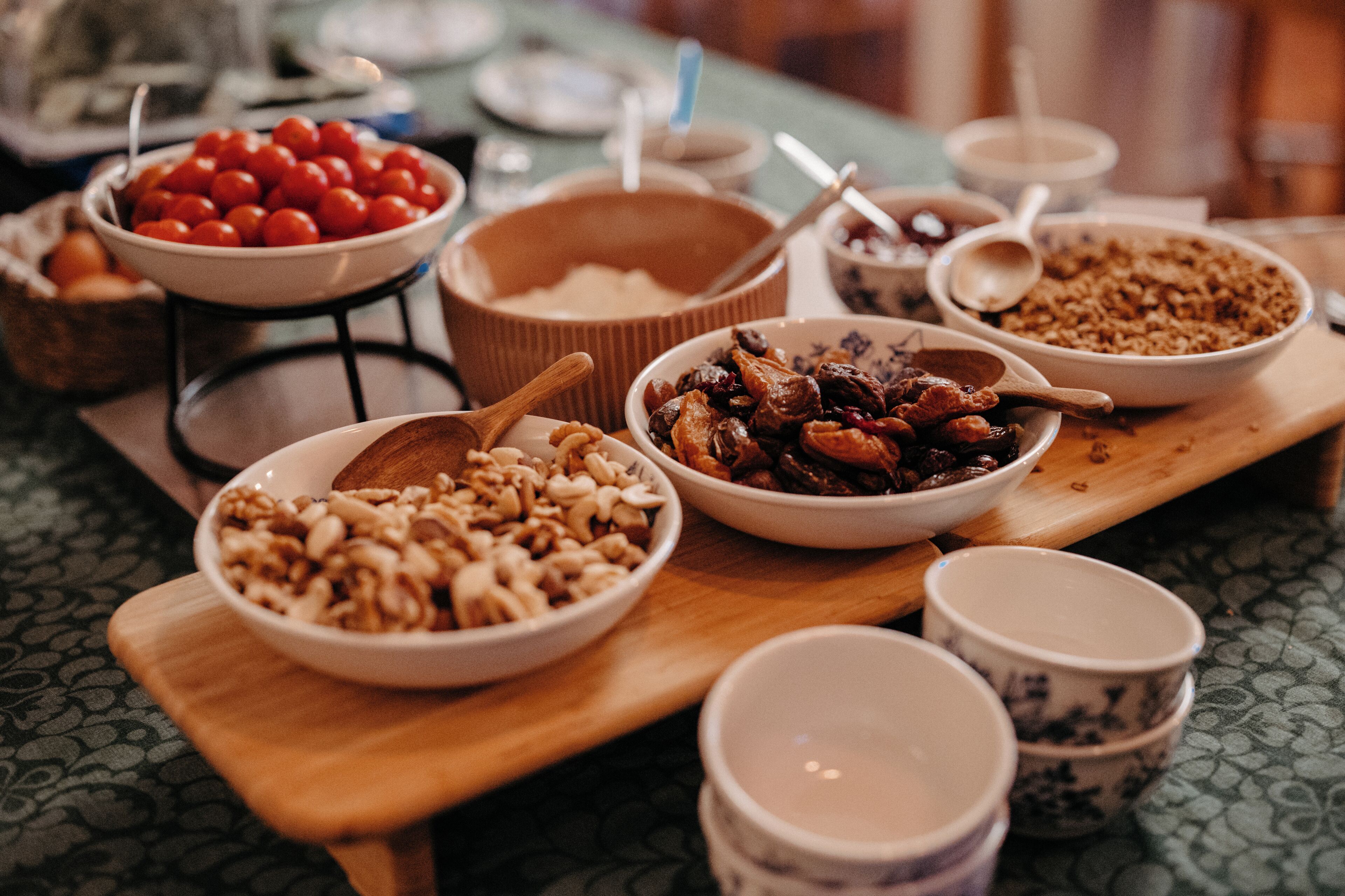 A variety of food items displayed on a wooden board, including bowls of nuts, dried fruits, and other snacks.