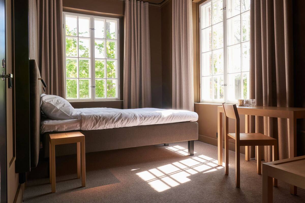 A bedroom with a bed, a desk, and two windows.