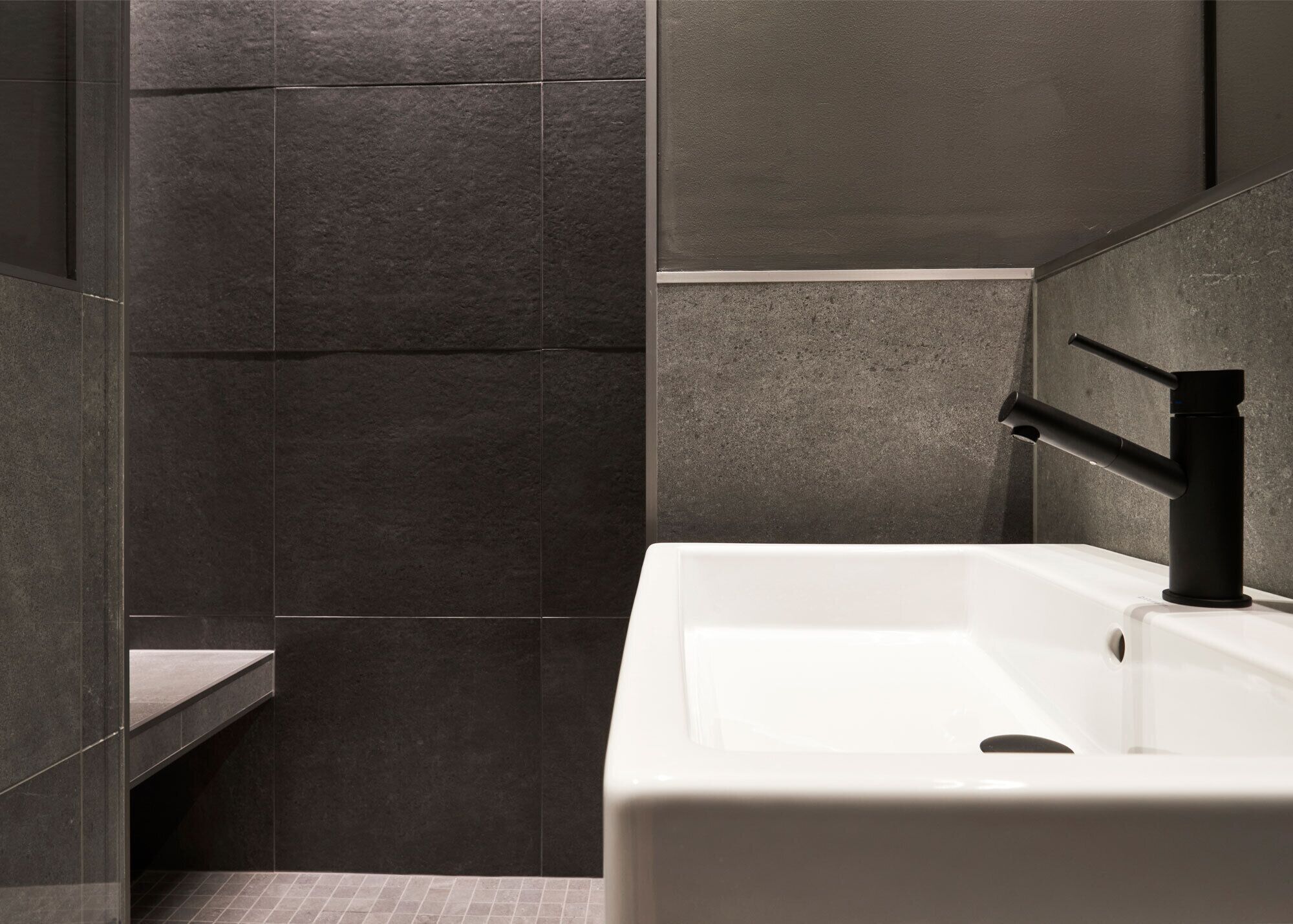 Un baño moderno con un lavamanos blanco y un grifo negro, rodeado de baldosas de piedra oscura.