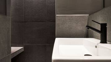 Une salle de bain moderne avec un lavabo blanc et un robinet noir, le tout entouré de carreaux de pierre foncée.