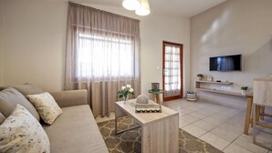 A living room with a sofa, a coffee table, a TV, and a dining area. - apartment C - Red Apartment (Vir)