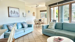 Un salon avec deux canapés bleu clair, une table à manger avec des chaises et une grande fenêtre donnant sur l’extérieur.