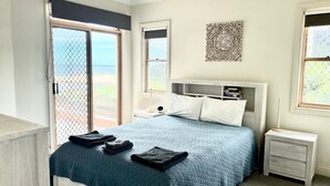 Une chambre à coucher comprenant un lit, deux tables de chevet, une commode et une fenêtre donnant sur un paysage agréable.