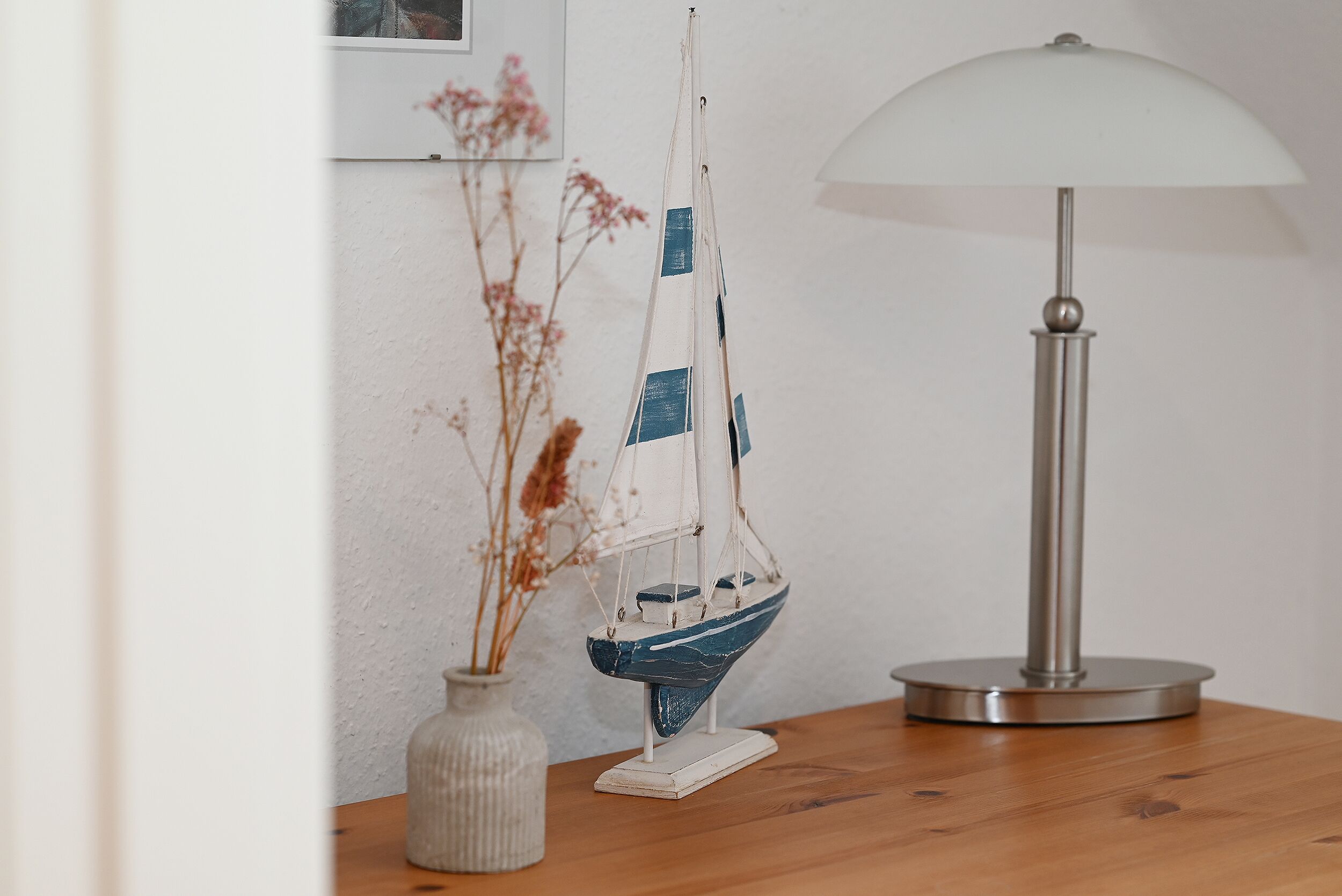 A small model sailboat on a wooden table next to a lamp.