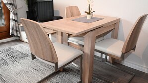 Un comedor con una mesa y sillas de madera, una pequeña planta en maceta y un televisor al fondo.