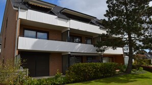 Un edificio residencial moderno de dos pisos con balcón, fachada de ladrillo y césped cuidado.