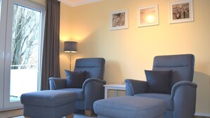 Una habitación con dos sillones azules, una mesita y un amplio ventanal con cortinas.