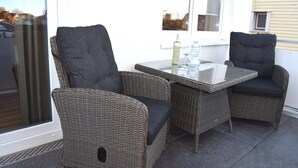 Un patio con muebles de mimbre y una mesa de vidrio, con una botella y copas.